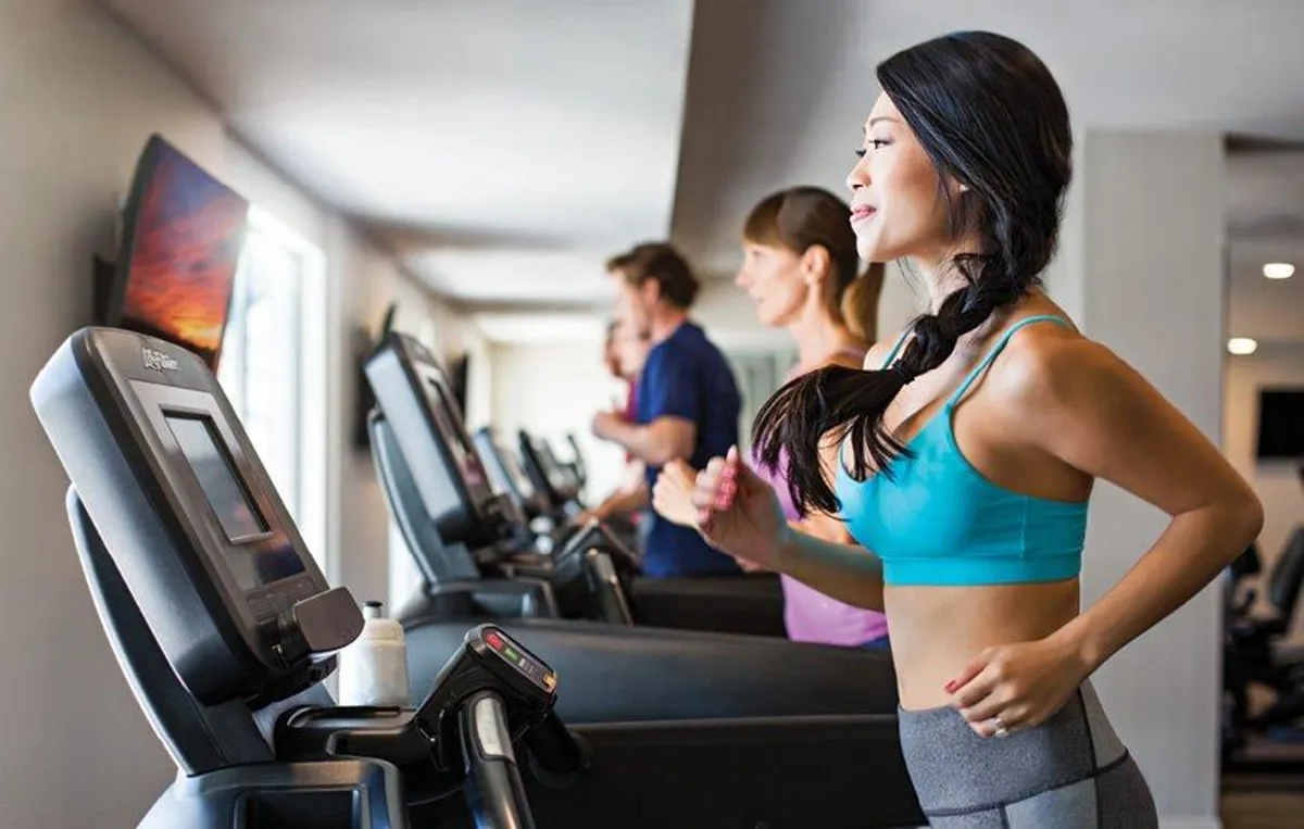 A modern fitness center featuring treadmills, people actively exercising, and a television screen. The space is bright and motivating, encouraging healthy habits and interaction among residents.