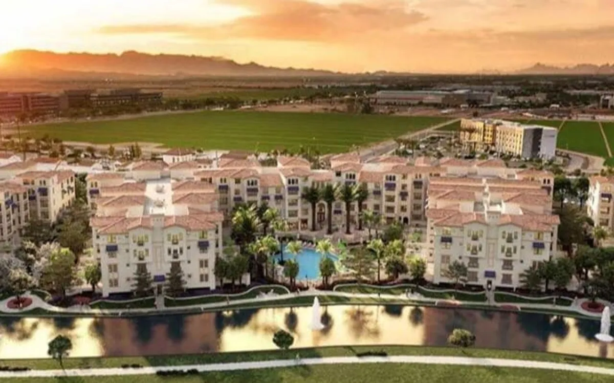 A wide view of the community's swimming pool framed by palm trees, with landscaped gardens, a fountain, and the apartment buildings in the background. Open green fields invite relaxation and casual strolls, while lounge chairs and the tranquil water create a resort-like setting.