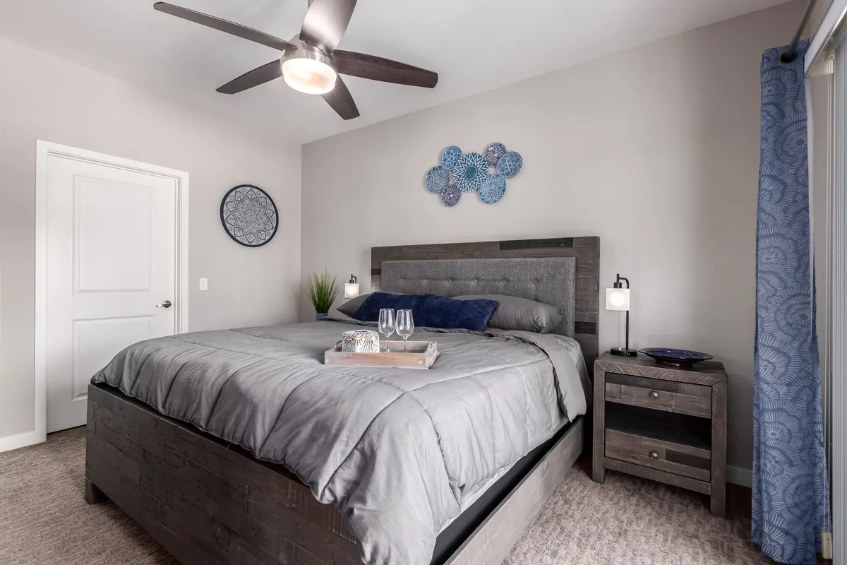 A calm and restful bedroom featuring a king-sized bed with plush linens, a nightstand, decorative wall art adding tranquility, and a ceiling fan above. The overall mood is peaceful and inviting, ideal for relaxation or enjoying a quiet evening with a book or watching TV.