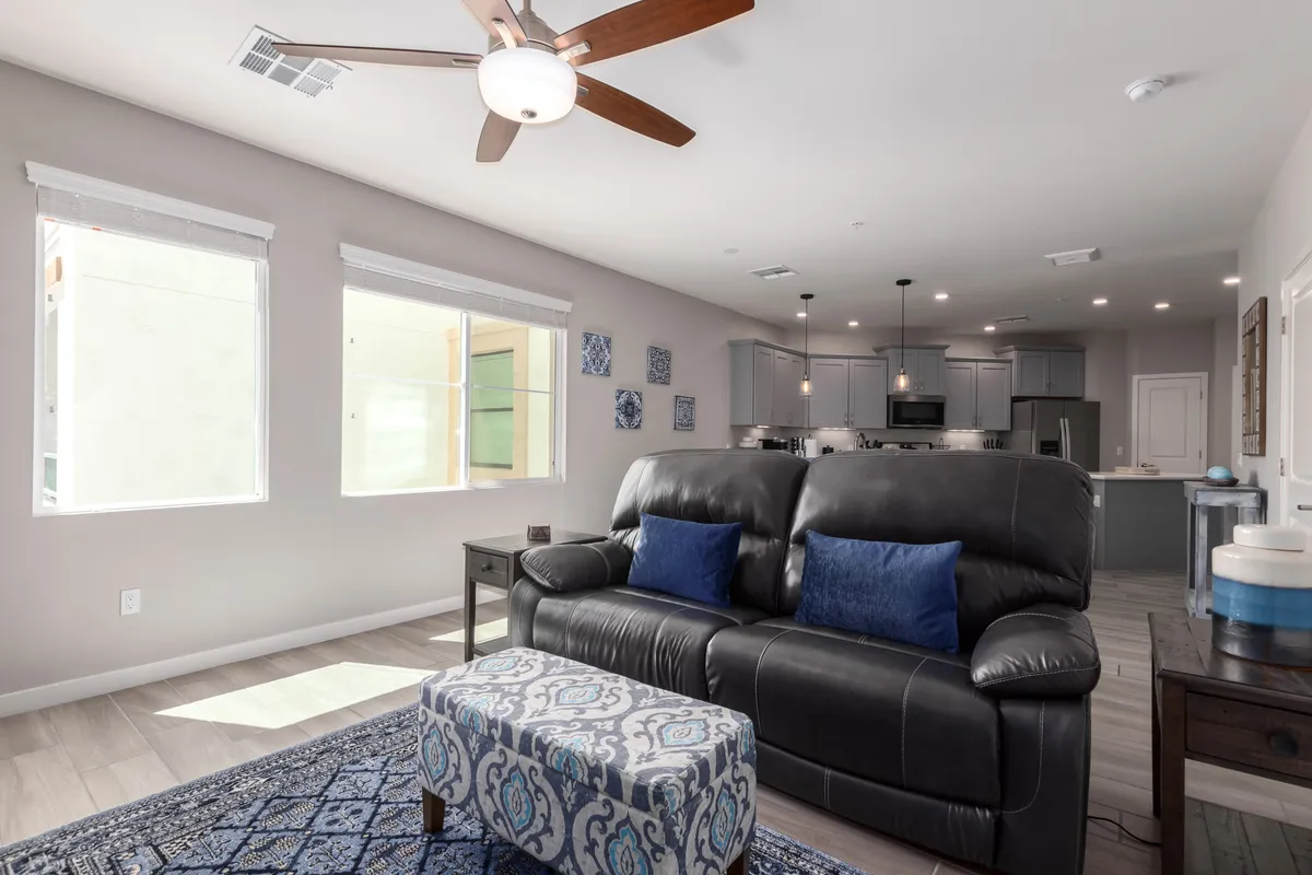 A welcoming open-plan living area featuring a leather sofa, decorative ottoman, stylish wall art, and a kitchen in the background. The space is ideal for relaxation, entertaining, and gathering with family or friends.