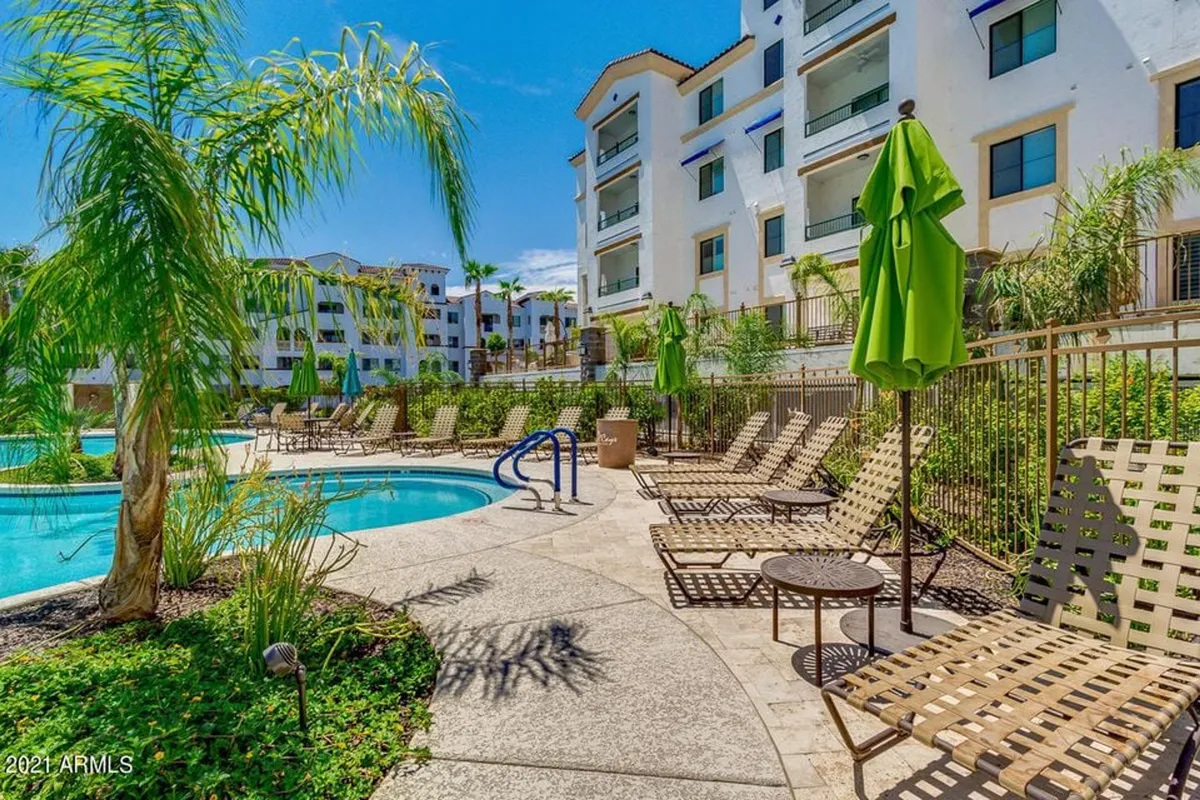 A sunny exterior shot of the swimming pool surrounded by comfortable lounge chairs and green umbrellas. Lush landscape greenery frames the pool, evoking a leisurely and inviting resort-style atmosphere. The image suggests a perfect spot for afternoon relaxation, sunbathing, or a casual dip, with the tranquil pool area hinting at privacy and indulgence.
