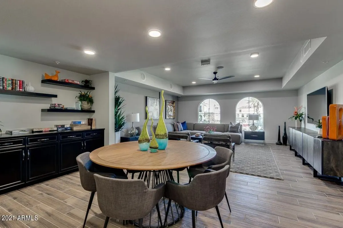 A bright, cozy room featuring a round dining table near large windows, bookshelves with decor, and a comfortable seating area. The space is filled with natural light and looks out onto the landscaped grounds, giving a seamless connection between indoor comforts and outdoor beauty.