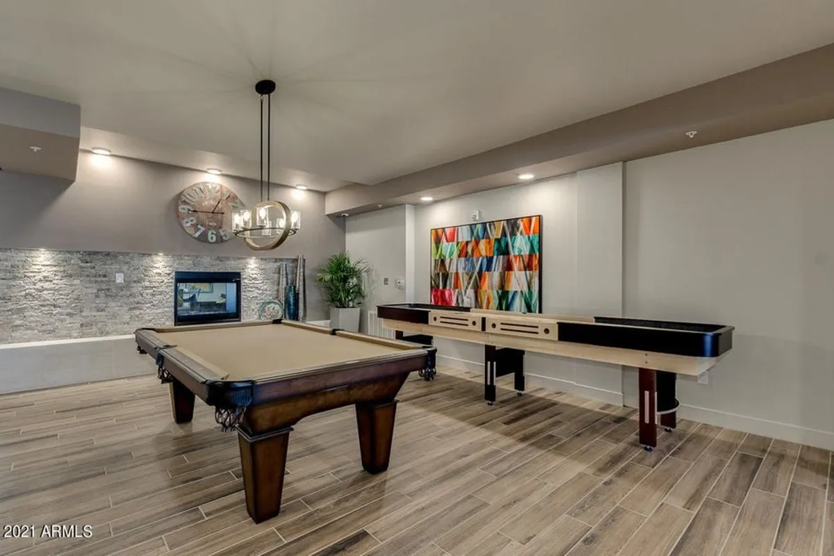 A stylish clubhouse interior with a pool table, shuffleboard, colorful wall art, and a cozy fireplace. The space is designed for socializing, games, and relaxing by the fire, capturing the energy and amenities of a modern clubhouse.
