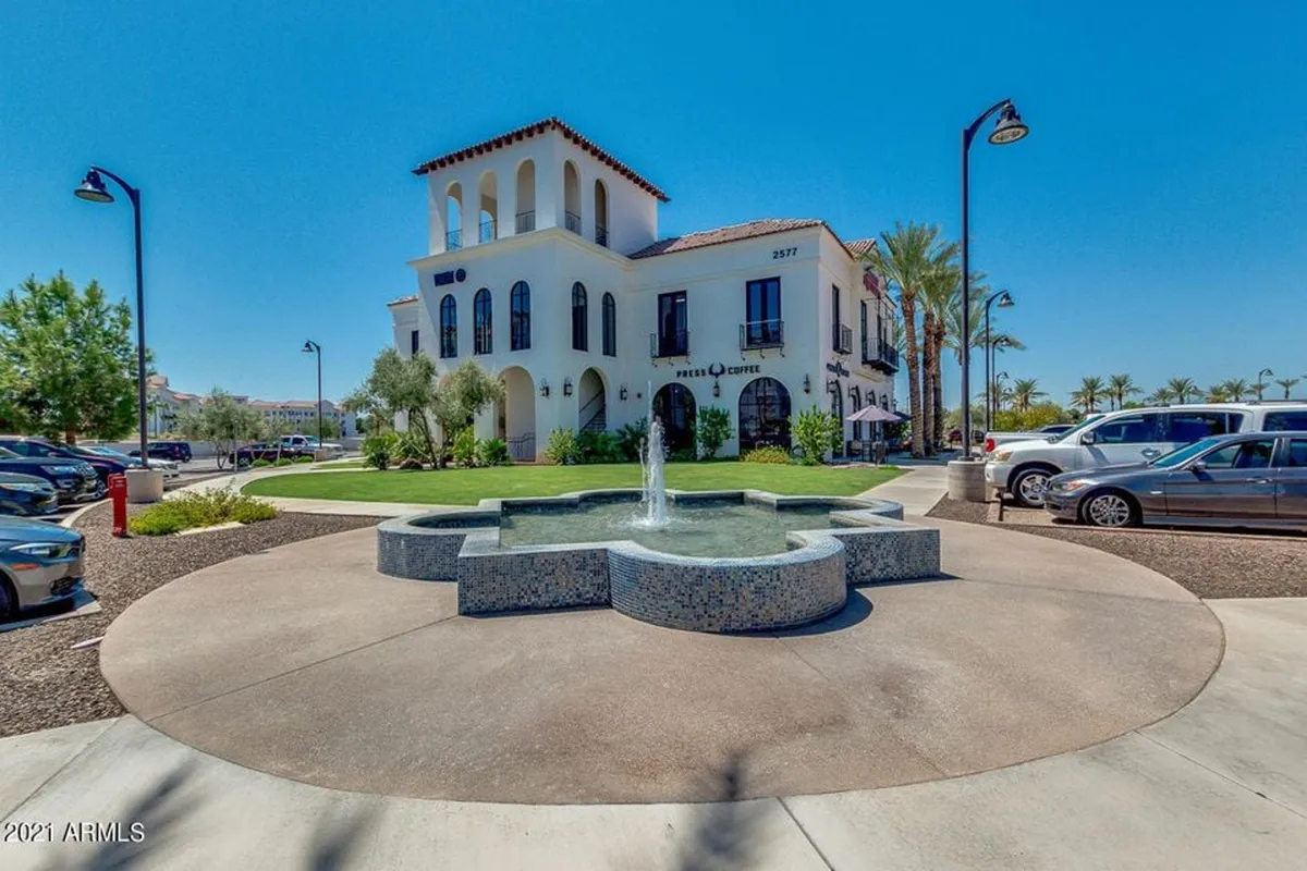 The elegant building facade of The Cays with a central fountain surrounded by lush landscaping. Residents relax by the fountain and outdoor seating areas, enjoying the inviting, resort-inspired environment.